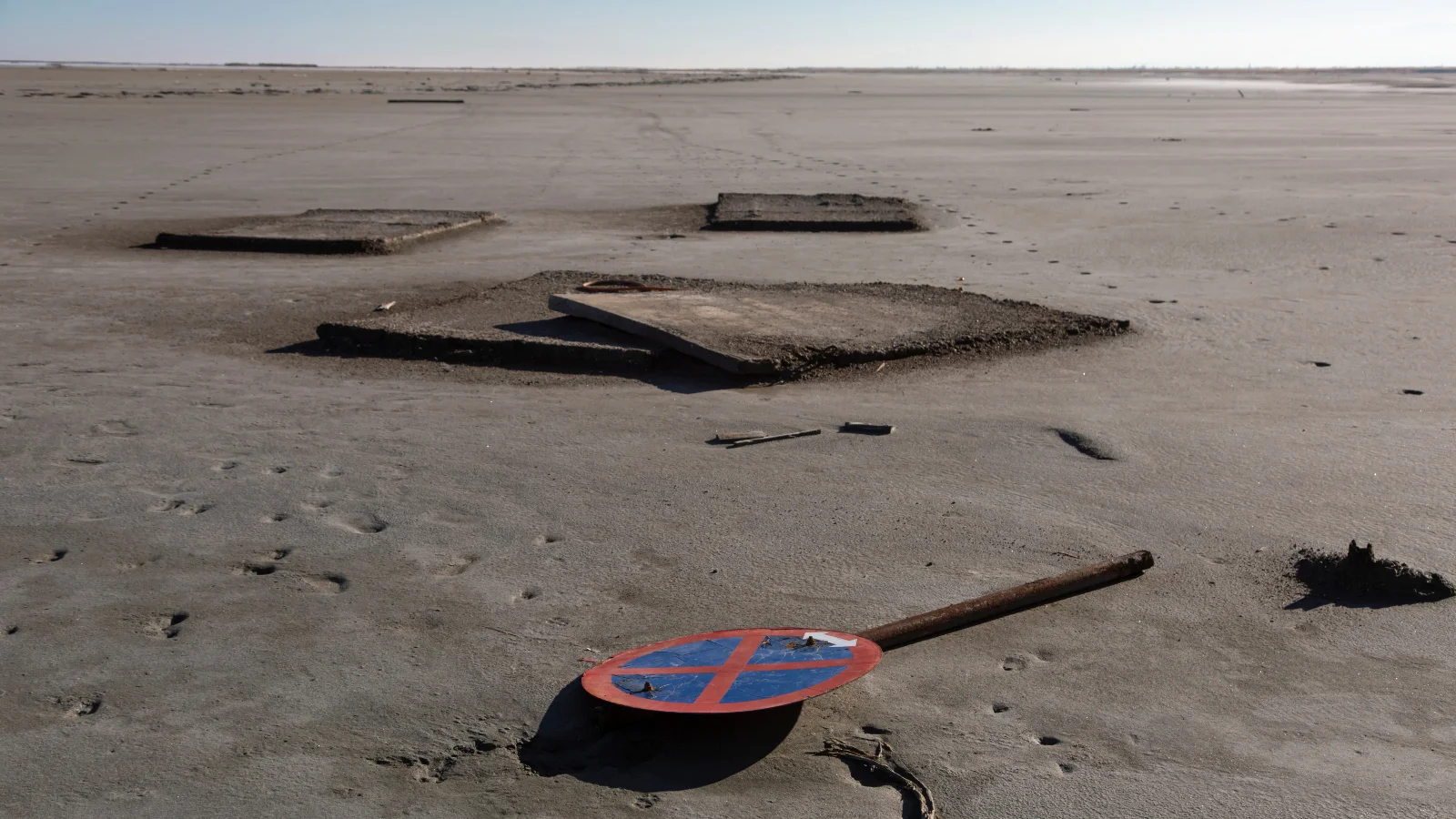 Photo of a discarded no-entry traffic sign lying on land parched by drought.
