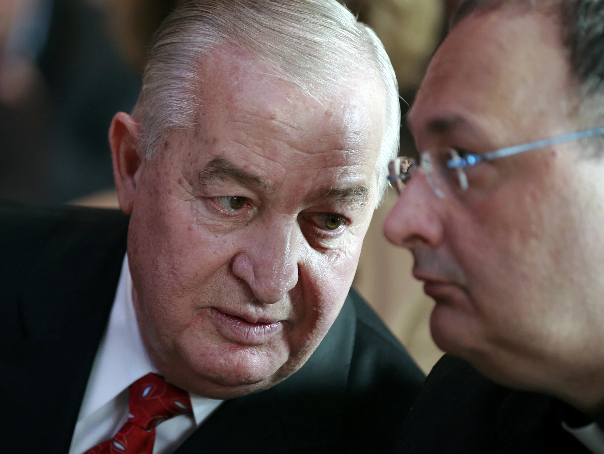 Louis DeNaples, wearing a suit and tie, leans over to speak to a man next to him.