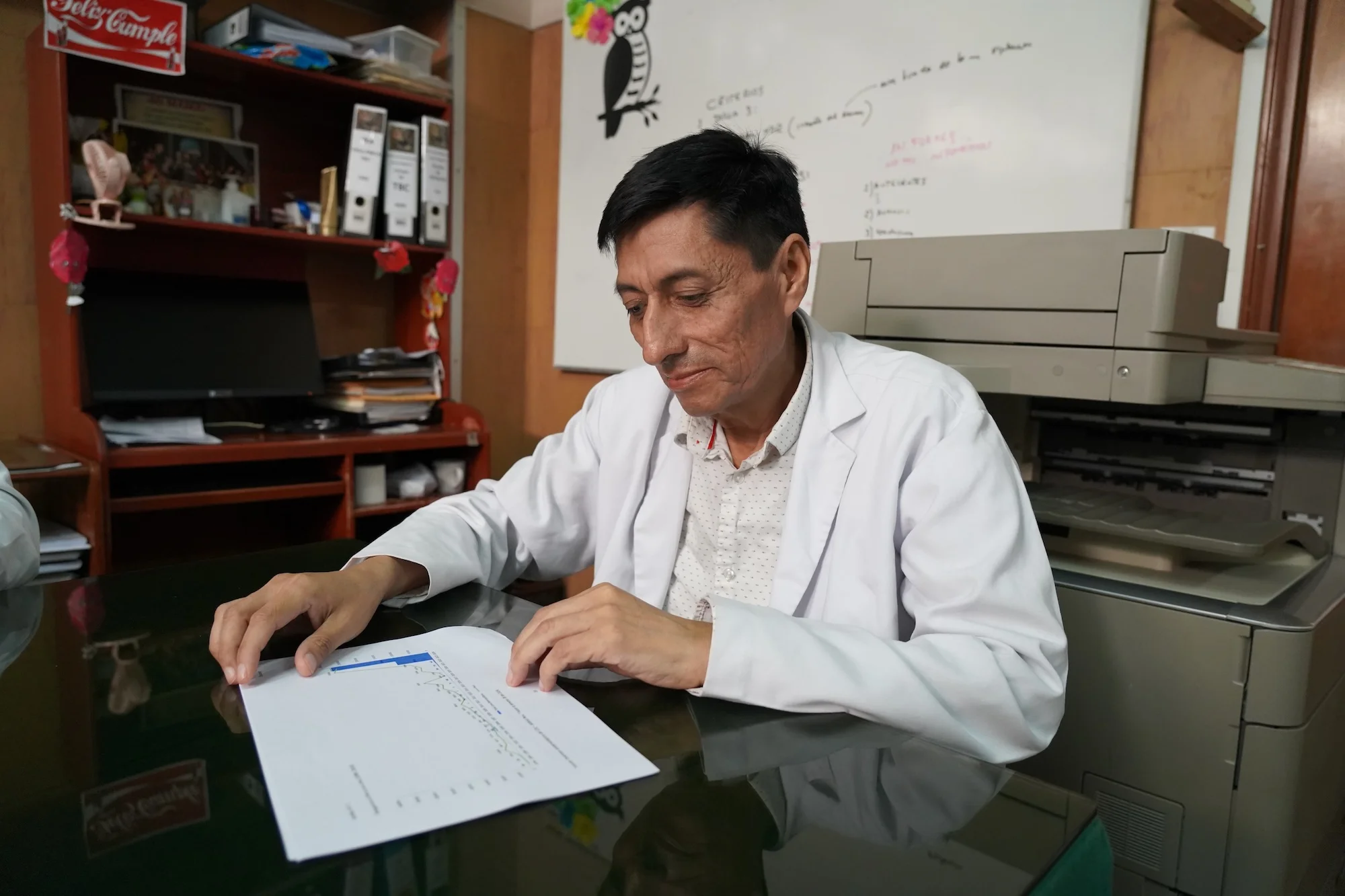 A man in a white doctor's coat looks at a piece of paper in a medical office
