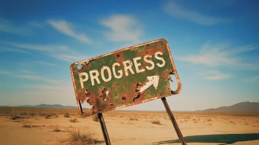 A weathered metal sign reading "PROGRESS" with an arrow stands in a barren desert landscape under a blue sky.