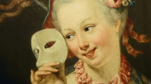A woman with flowers in her hair holds a white mask near her face and smiles, wearing a ruffled pink collar.